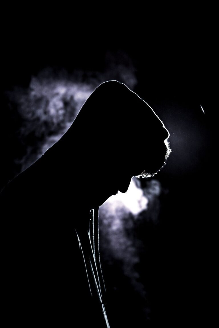 man in hood in smoke on black background