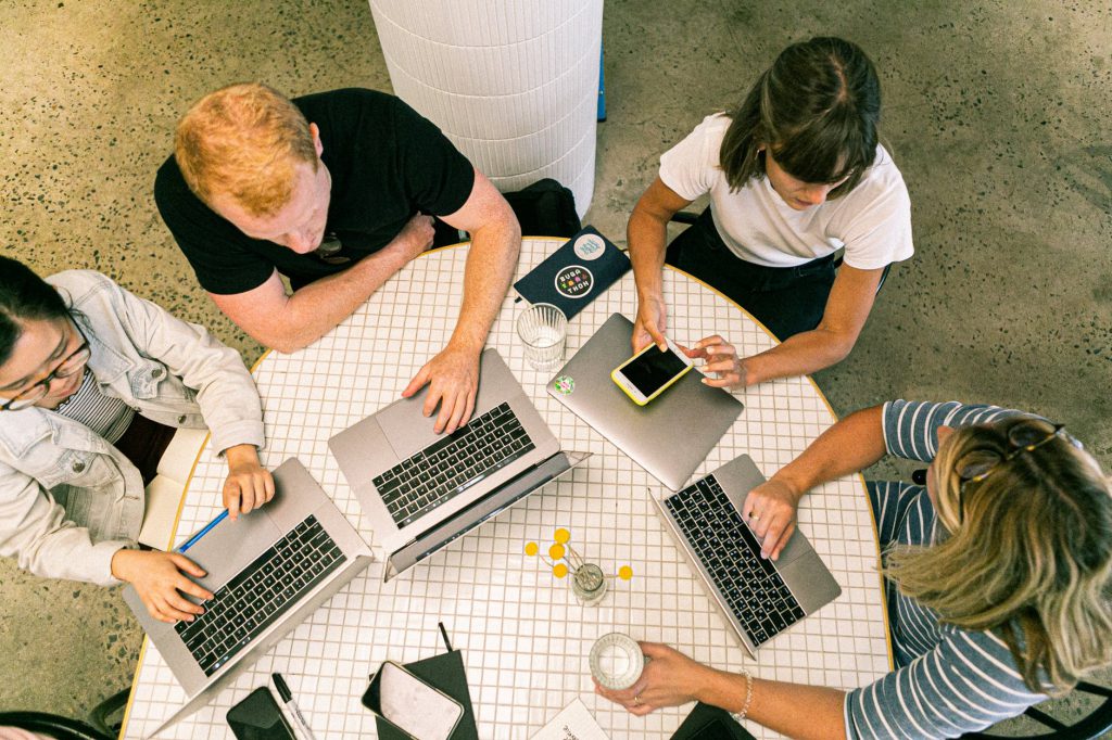 Reuni&atilde;o de quatro pessoas em torno de uma mesa, cada um com seu notebook. Foto por Canva Studio em Pexels.com