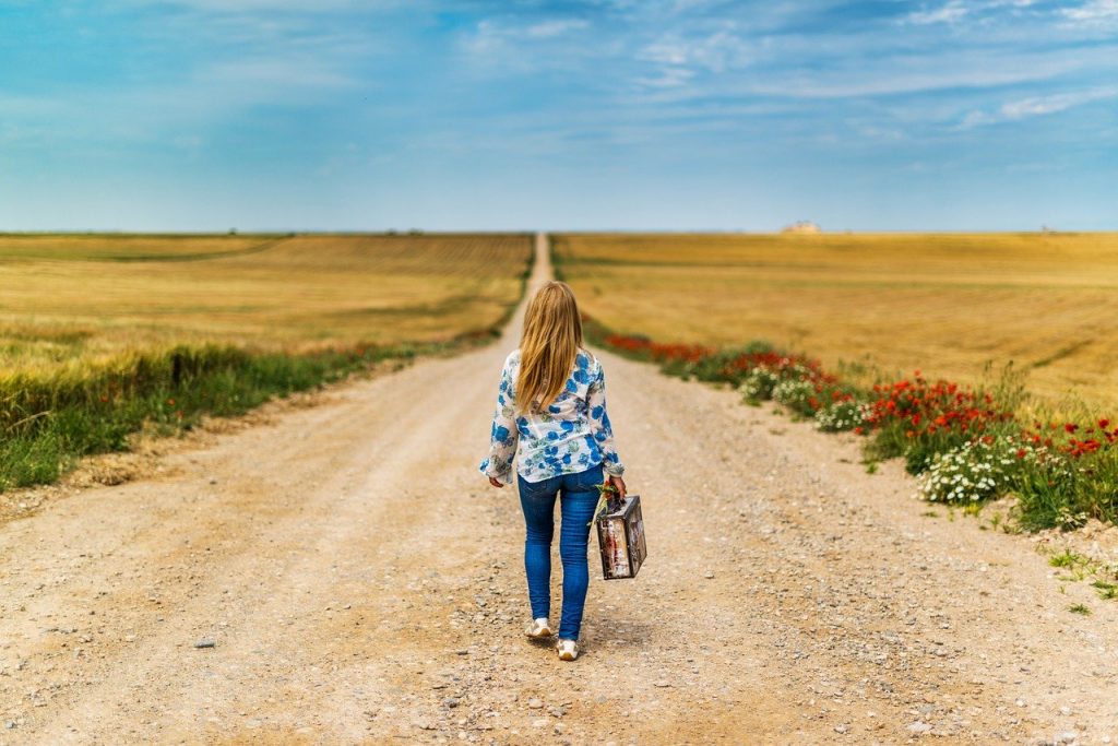 jovem andando por estrada de terra com uma mala