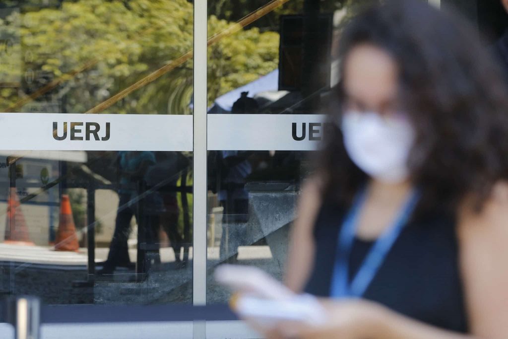 Destaque das notas econ&ocirc;micas:  foto de portaria da UFRJ com destaque para imagem de mulher olhando celuar 