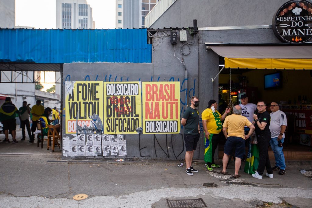 foto Felipe Campos Melo
Notas econ&ocirc;micas: grupo de apoiadores de bolsonaro conversa diante de bar e ao lado de faixas que protestam contra o governo