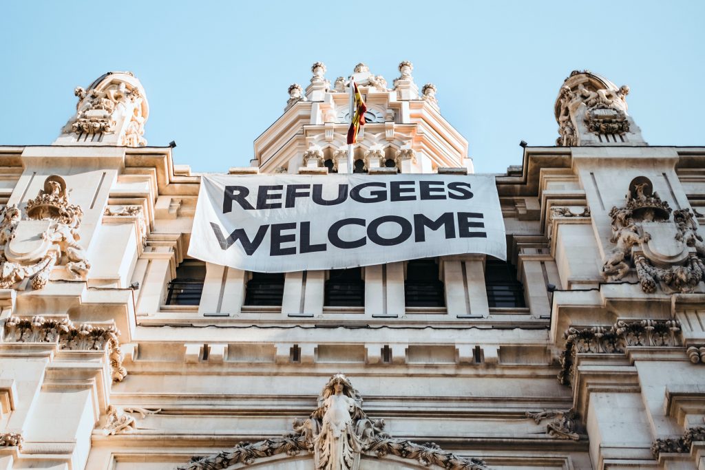 Photo by <a href="https://unsplash.com/@miteneva?utm_source=unsplash&utm_medium=referral&utm_content=creditCopyText">Maria Teneva</a> on <a href="https://unsplash.com/s/photos/no-war?utm_source=unsplash&utm_medium=referral&utm_content=creditCopyText">Unsplash</a>   
guerra fria e as v&iacute;timas de sempre: foto de pr&eacute;dio antigo, n&atilde;o identificado, com placa bem vindos refugiados
