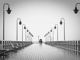 casal passeia em um pier em dia chuvoso