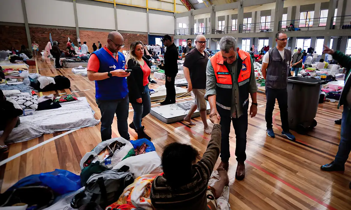 mais de 70 mil pessoas em abrigo no rio grande do sul Foto mostra pessoas desabrigadas, com colchões e roupas espalhadas por um grande salão. Foto: Cesar Lopes/PMPA
