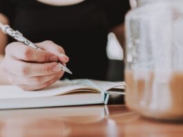 foto de pessoa não identificada escrevendo em caderno tendo uma vasilha com café diante dela